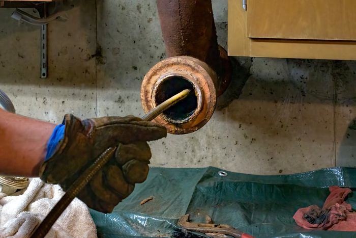 Hands of a plumber as he runs a camera scope and cleaning machine through the main pipe to unclog the drain